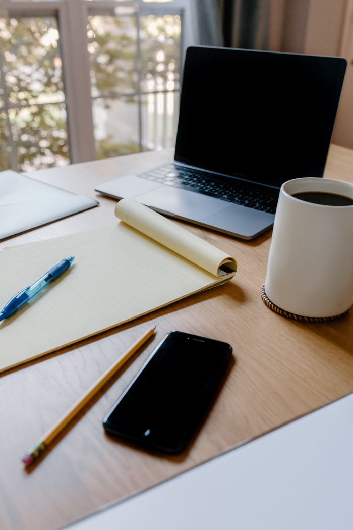 A cozy home office setup with a laptop, coffee, and notepad on a wooden desk.